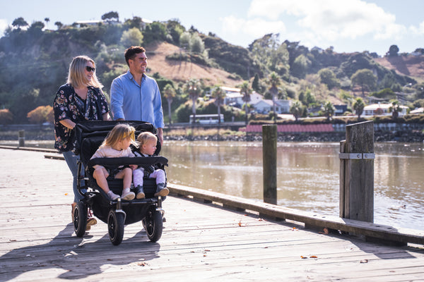 Family walking with two young children in a KinderPod double pushchair beside the waterfront