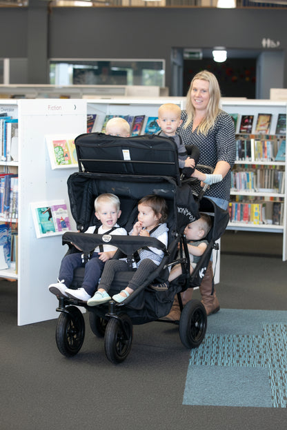 A multi-seat push chair with six children been pushed by a childminder in a library