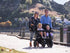 Family walking with two young children in a KinderPod double pushchair beside the waterfront.