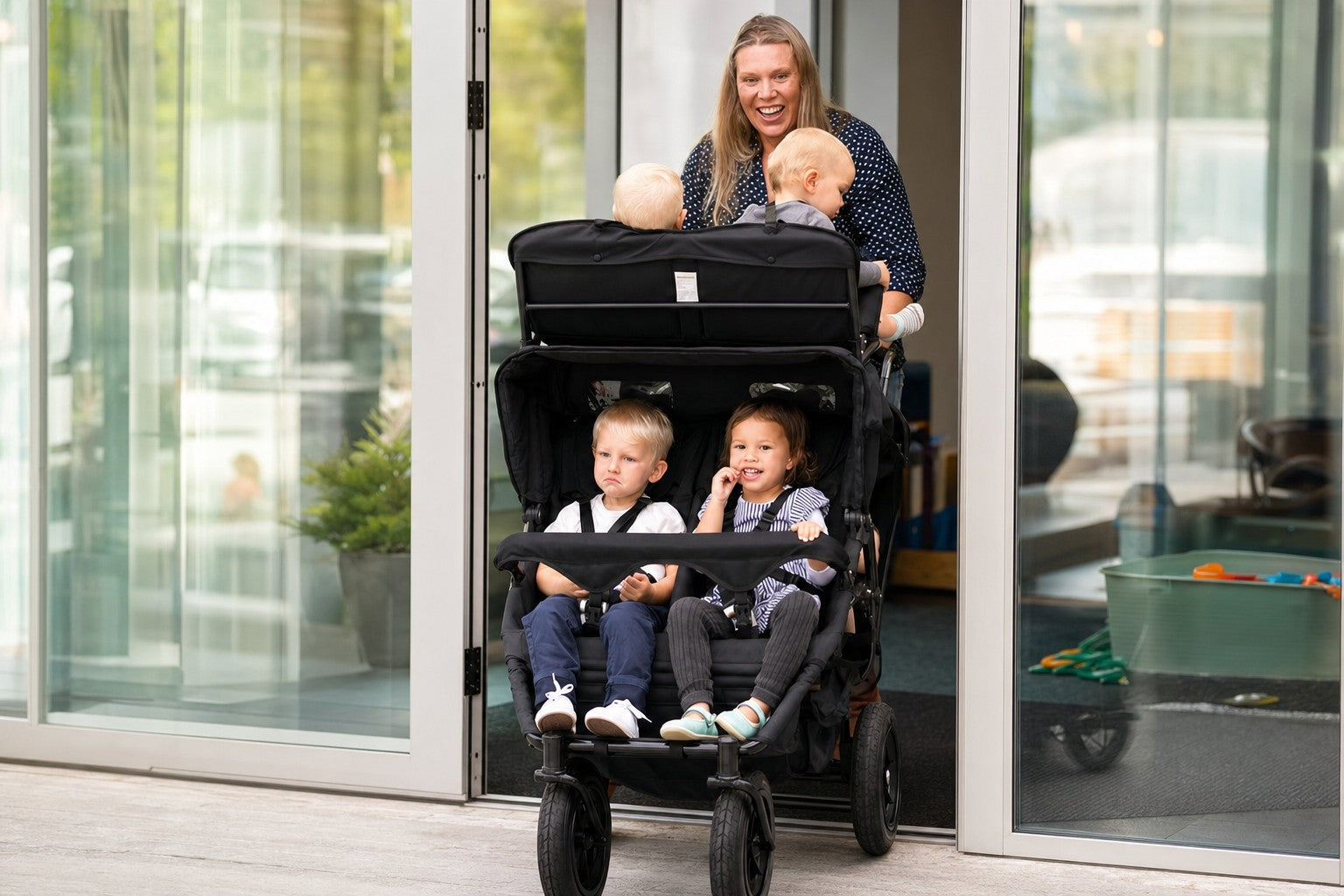 A parent pushing a KinderPod multi-seat stroller through a glass doorway